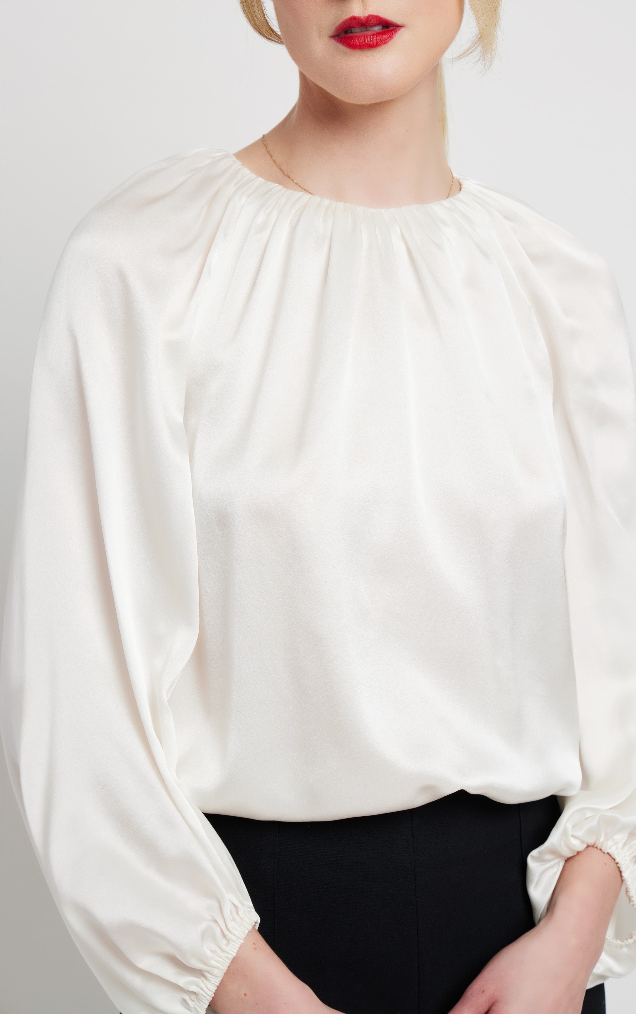 front close up of woman standing wearing silk white top with rusched neck and puff sleeve opening