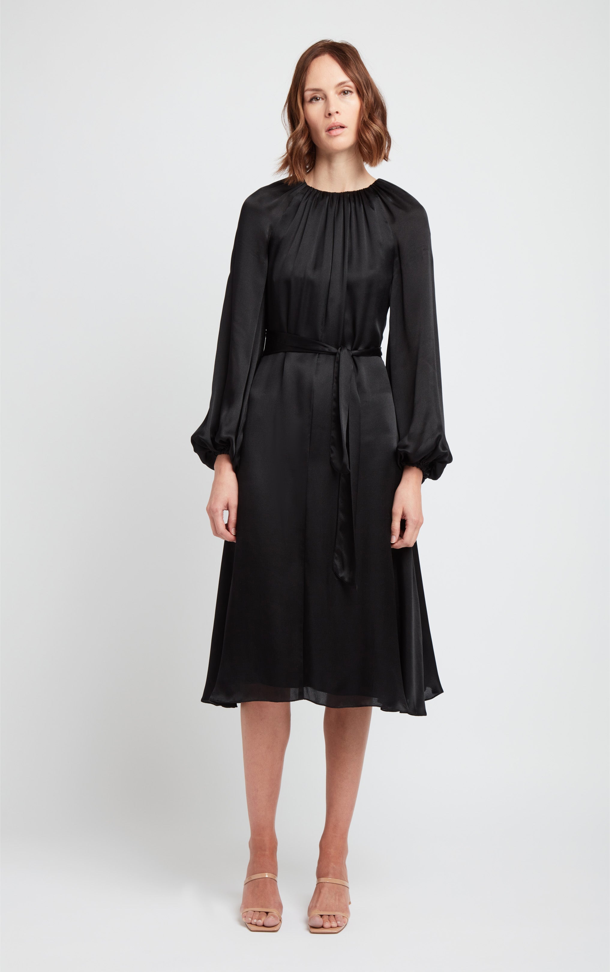 front view of woman wearing black puff sleeve silk dress with rusched neck