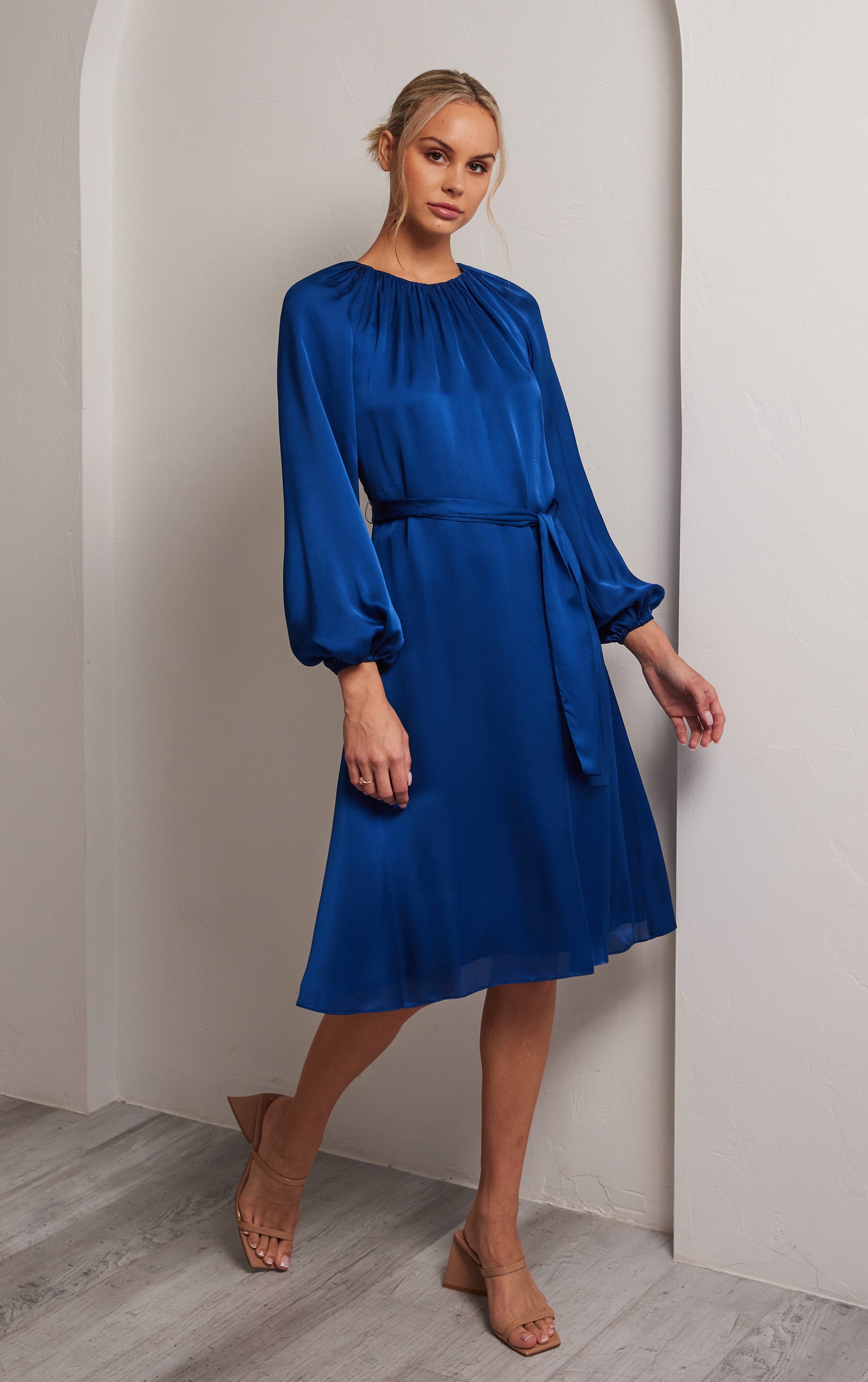 woman standing profile front view blue puff sleeve silk dress with rusched neck