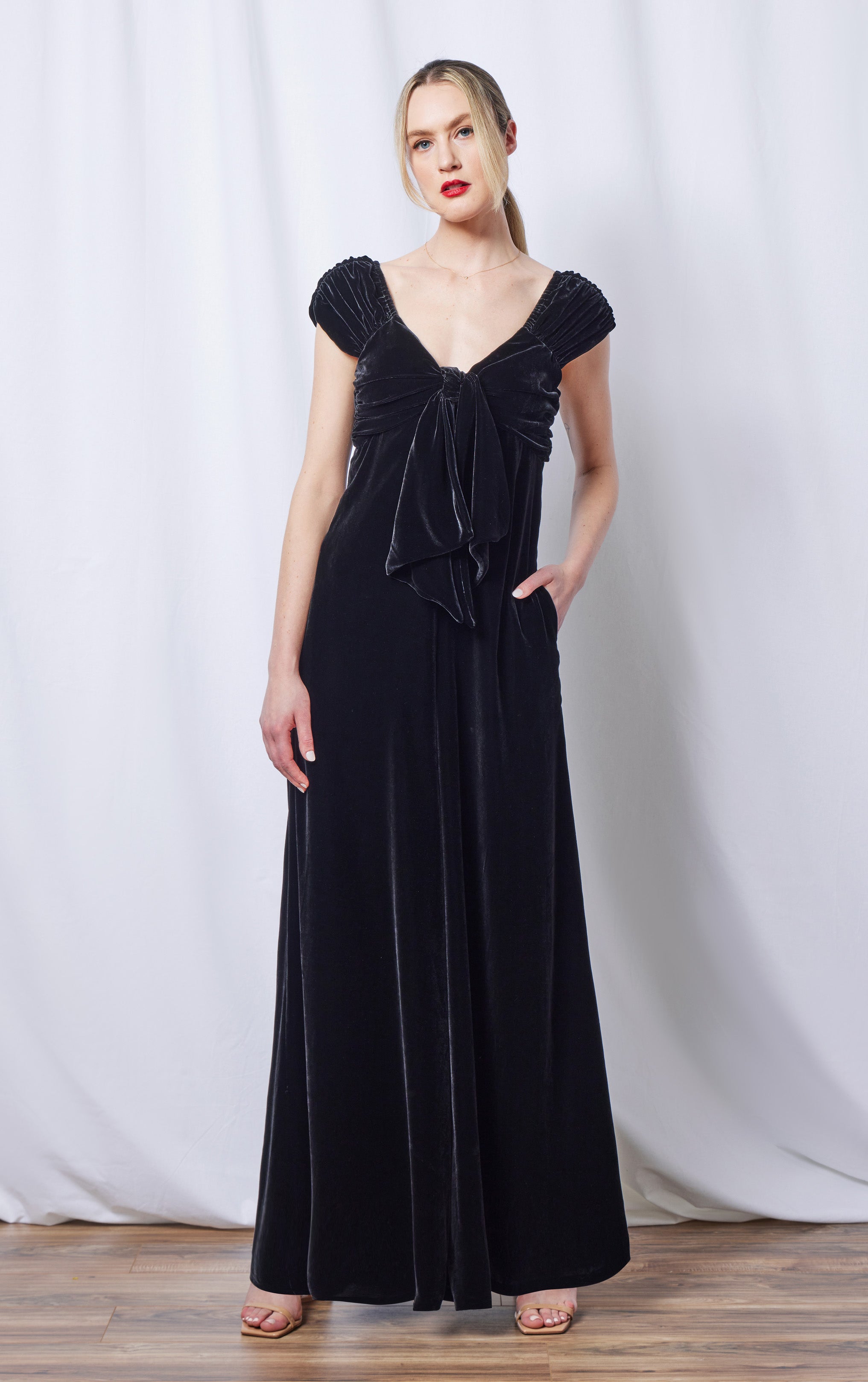 woman standing in front of curtain wearing silk velvet black jumpsuit with front bow