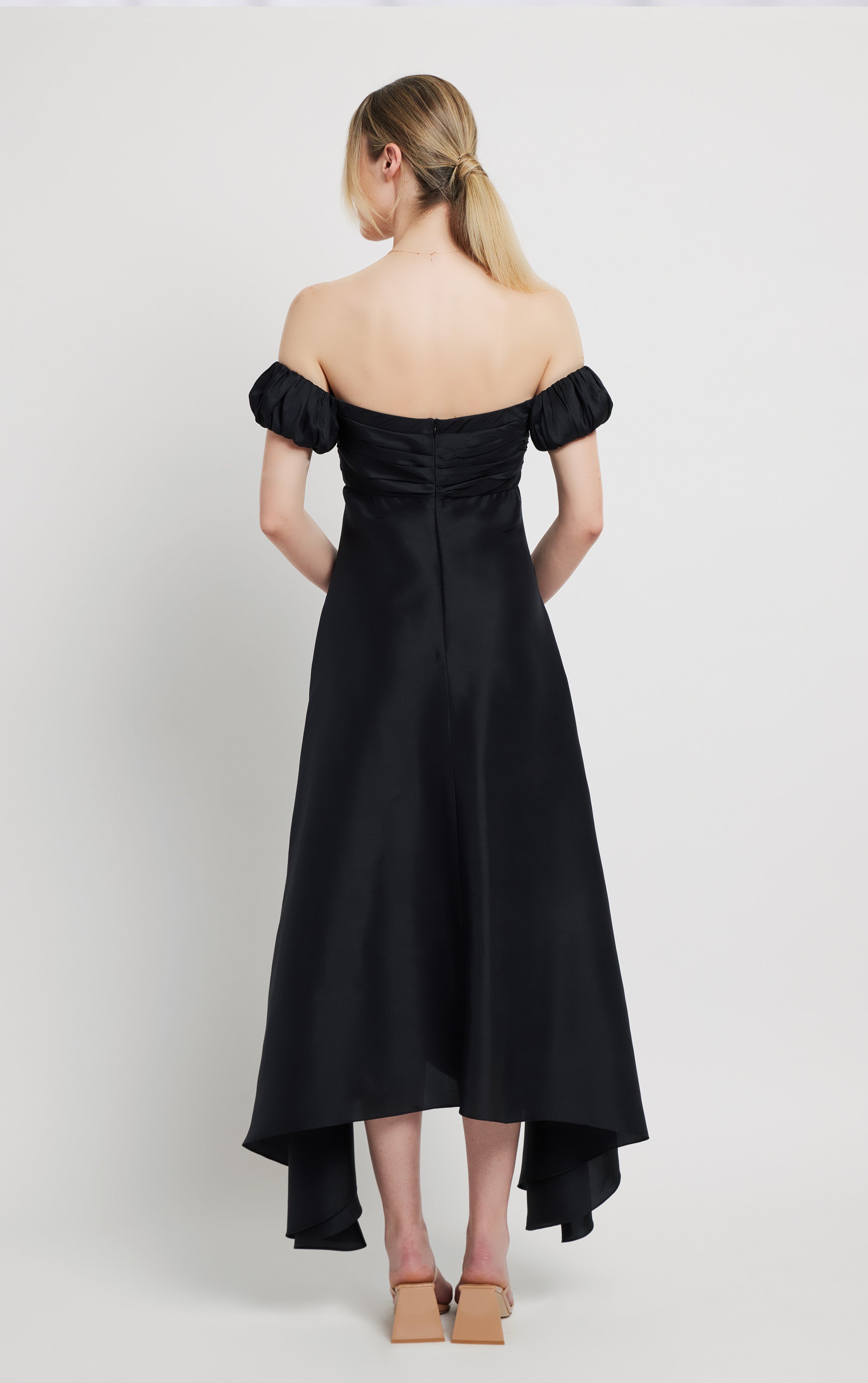 back view of woman standing wearing long silk black off the shoulder dress