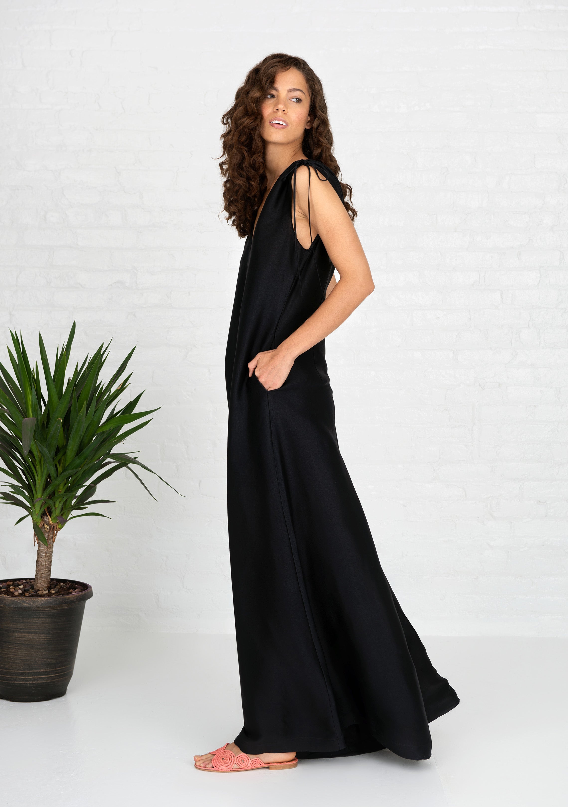 side profile of woman wearing black sleeveless silk jumpsuit with side hand pockets