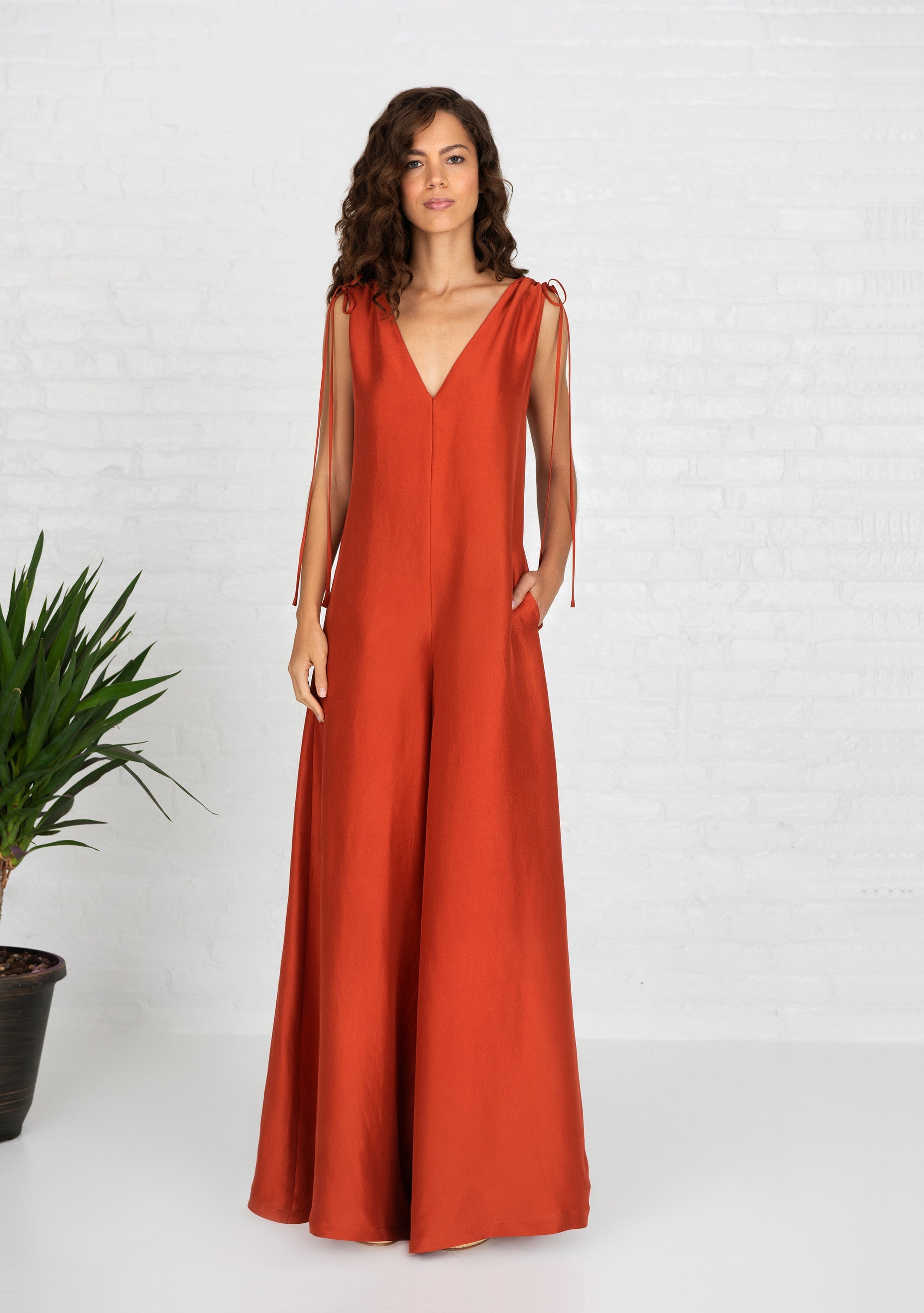 front view of woman wearing burnt orange sleeveless silk jumpsuit with side hand pockets