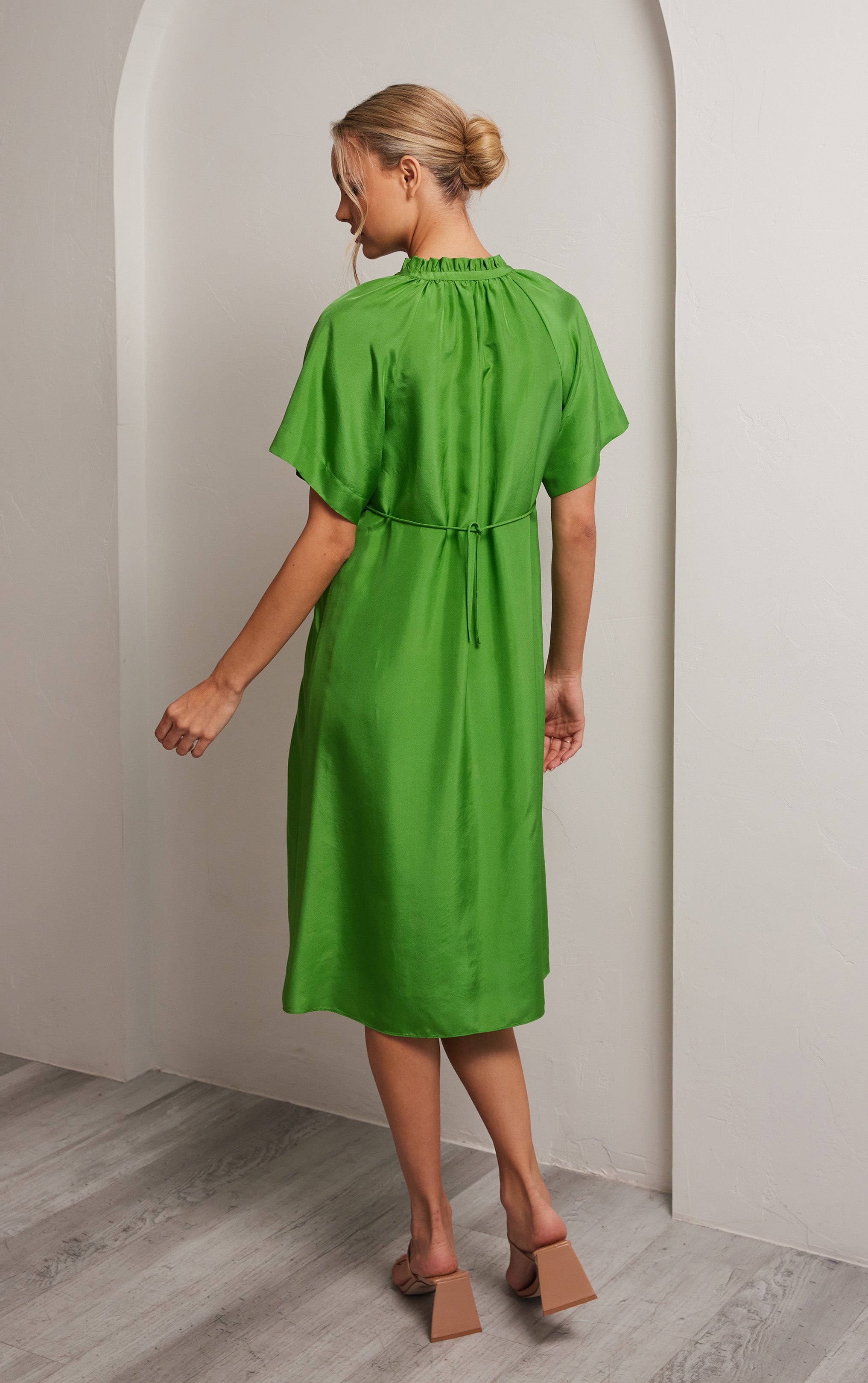 back view of woman wearing green short sleeved silk dress with ruffled neck trim and rusched neck