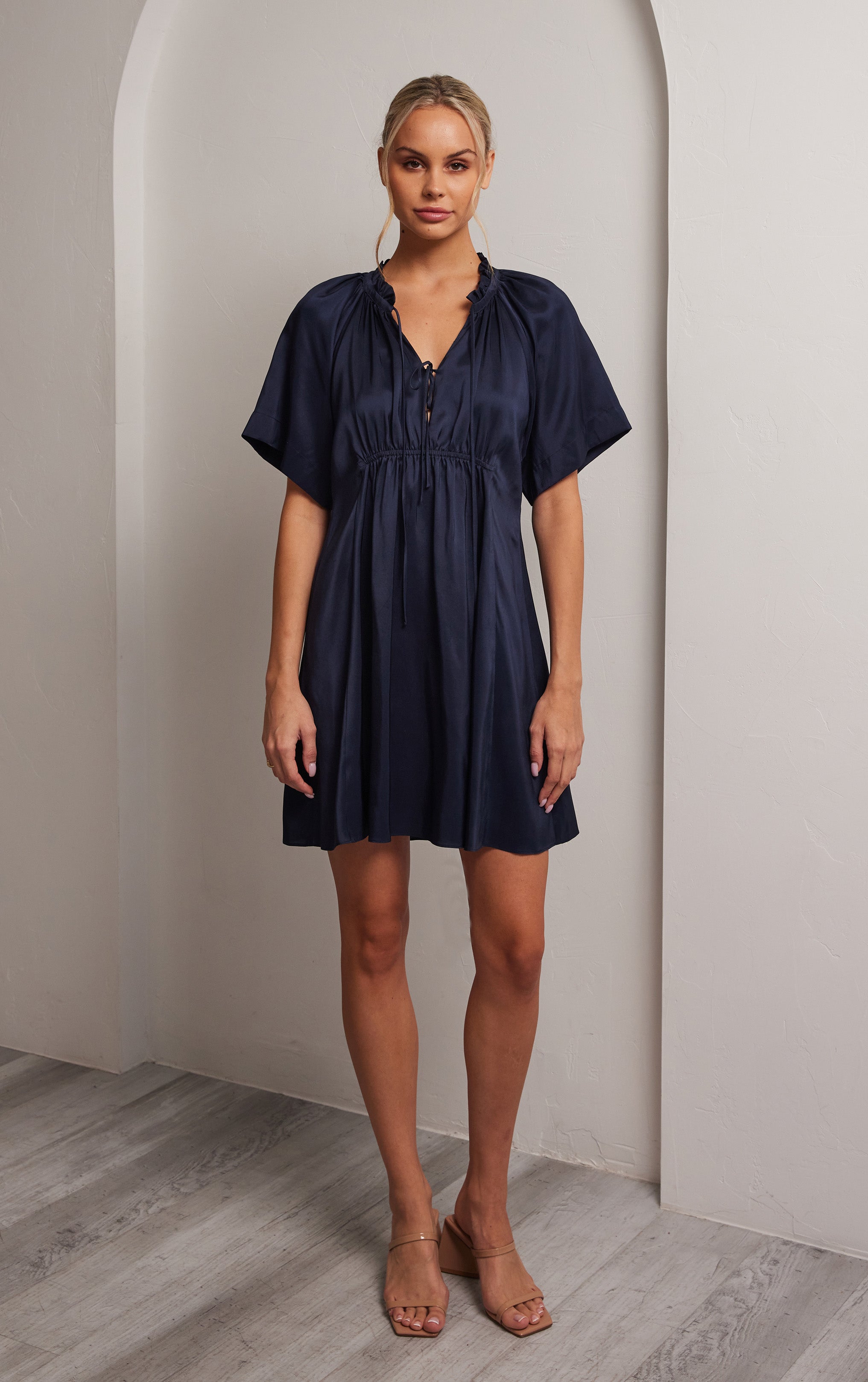 woman standing front view of navy short sleeved silk dress with ruffled neck and silhouette cut