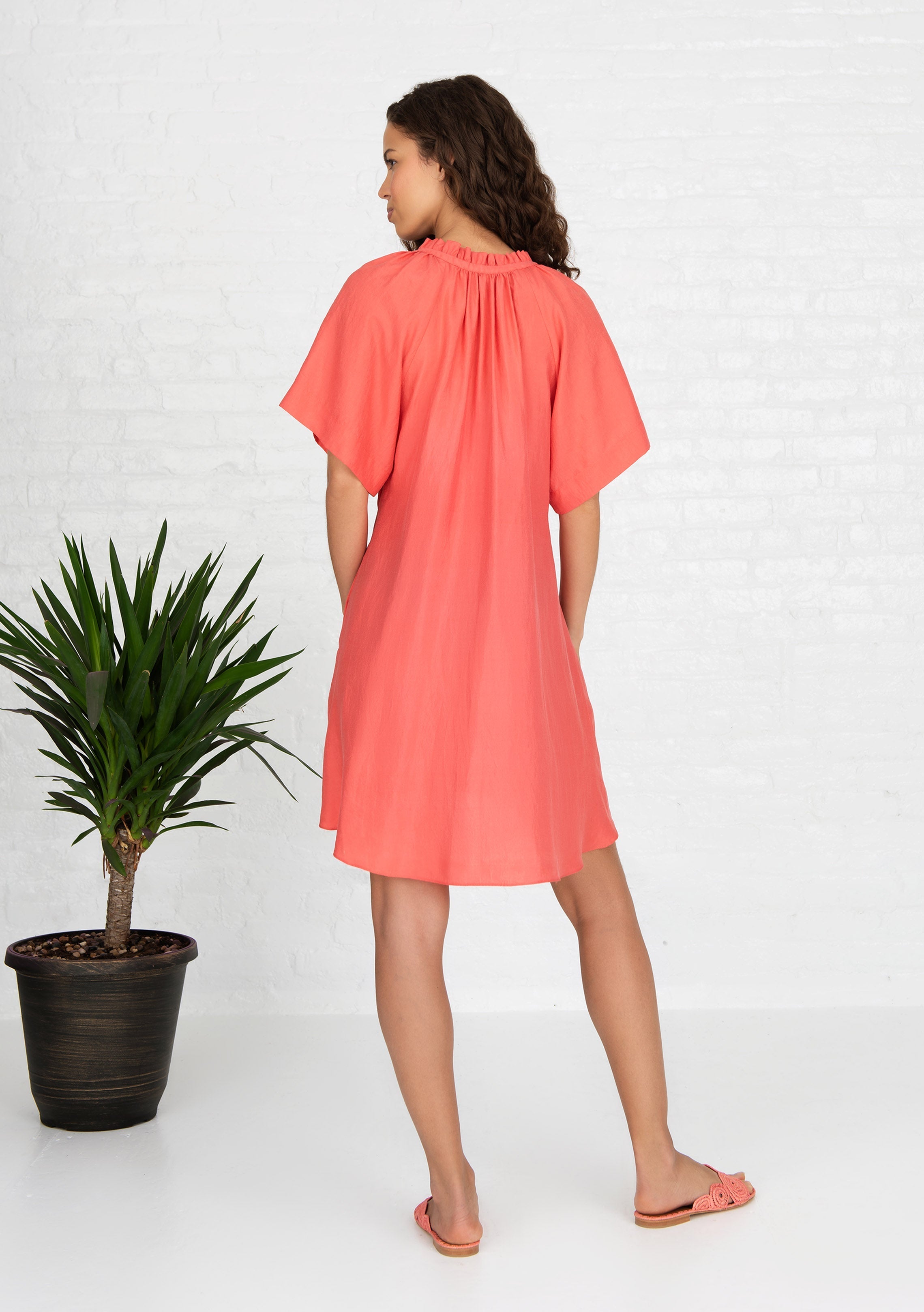 back profile view of woman wearing coral short sleeved silk dress handwoven