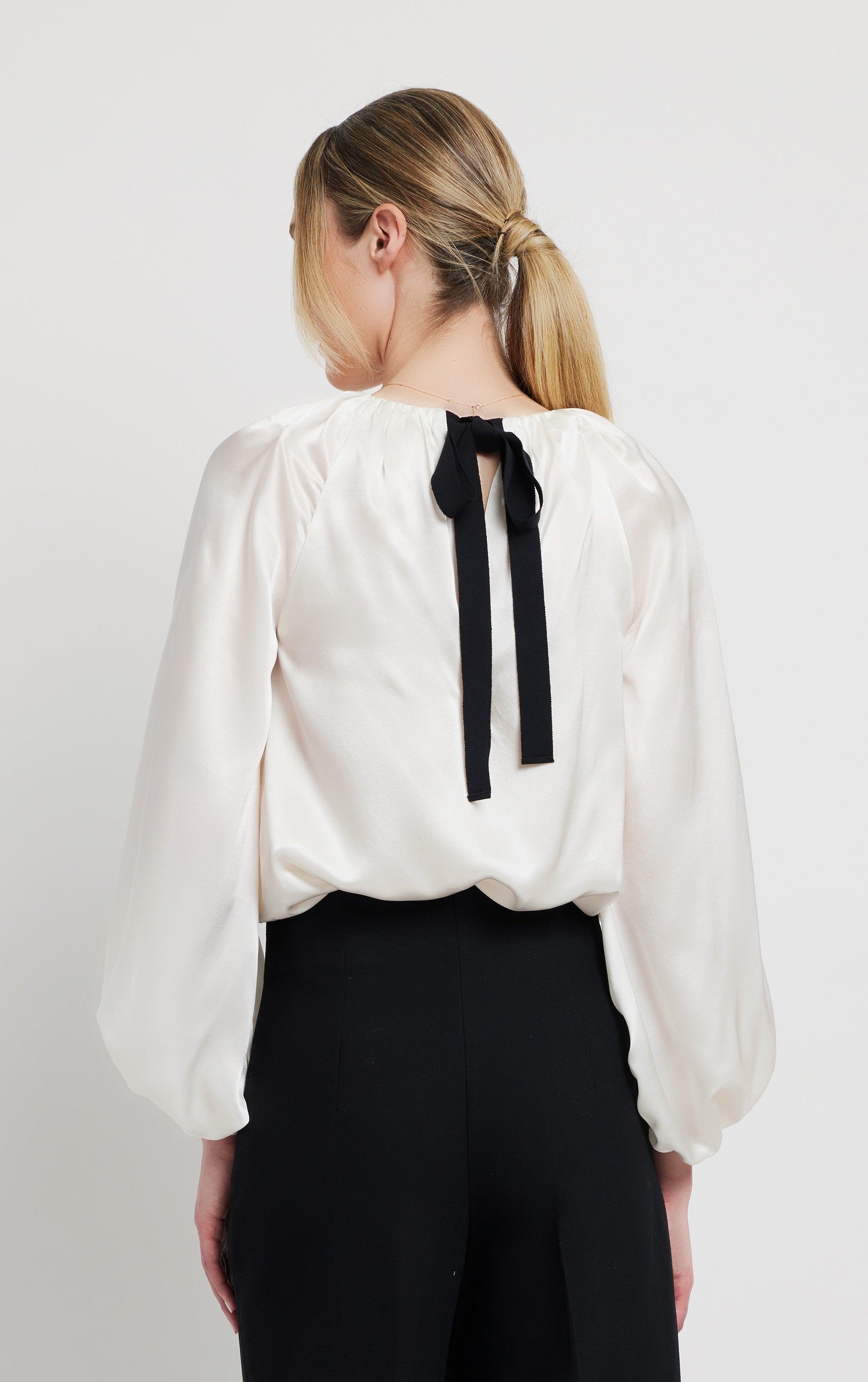 back profile view of woman wearing silk white top with rusched neck and puff sleeve opening