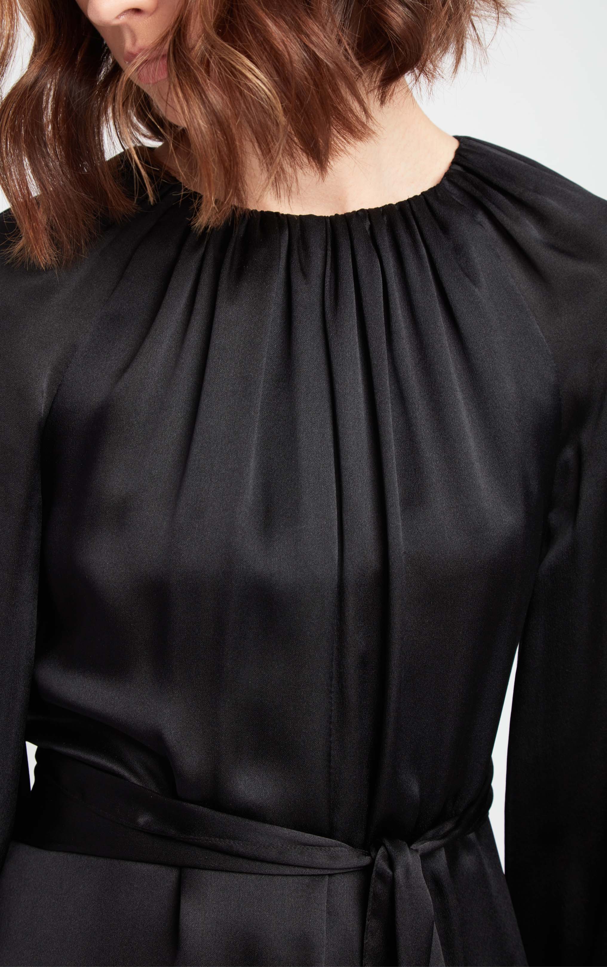 close up view of woman wearing black puff sleeve silk dress with rusched neck