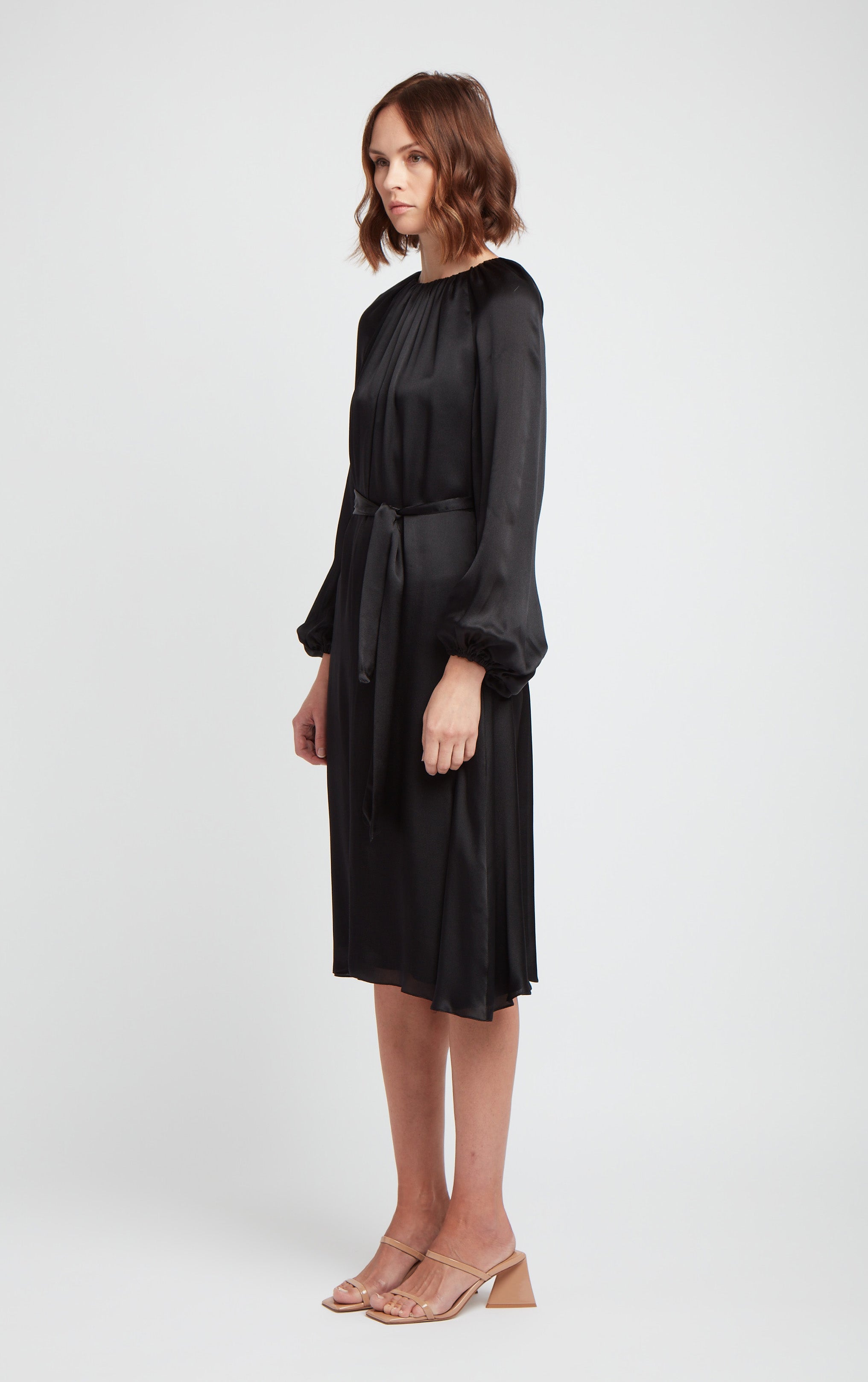 front and side view of woman wearing black puff sleeve silk dress with rusched neck