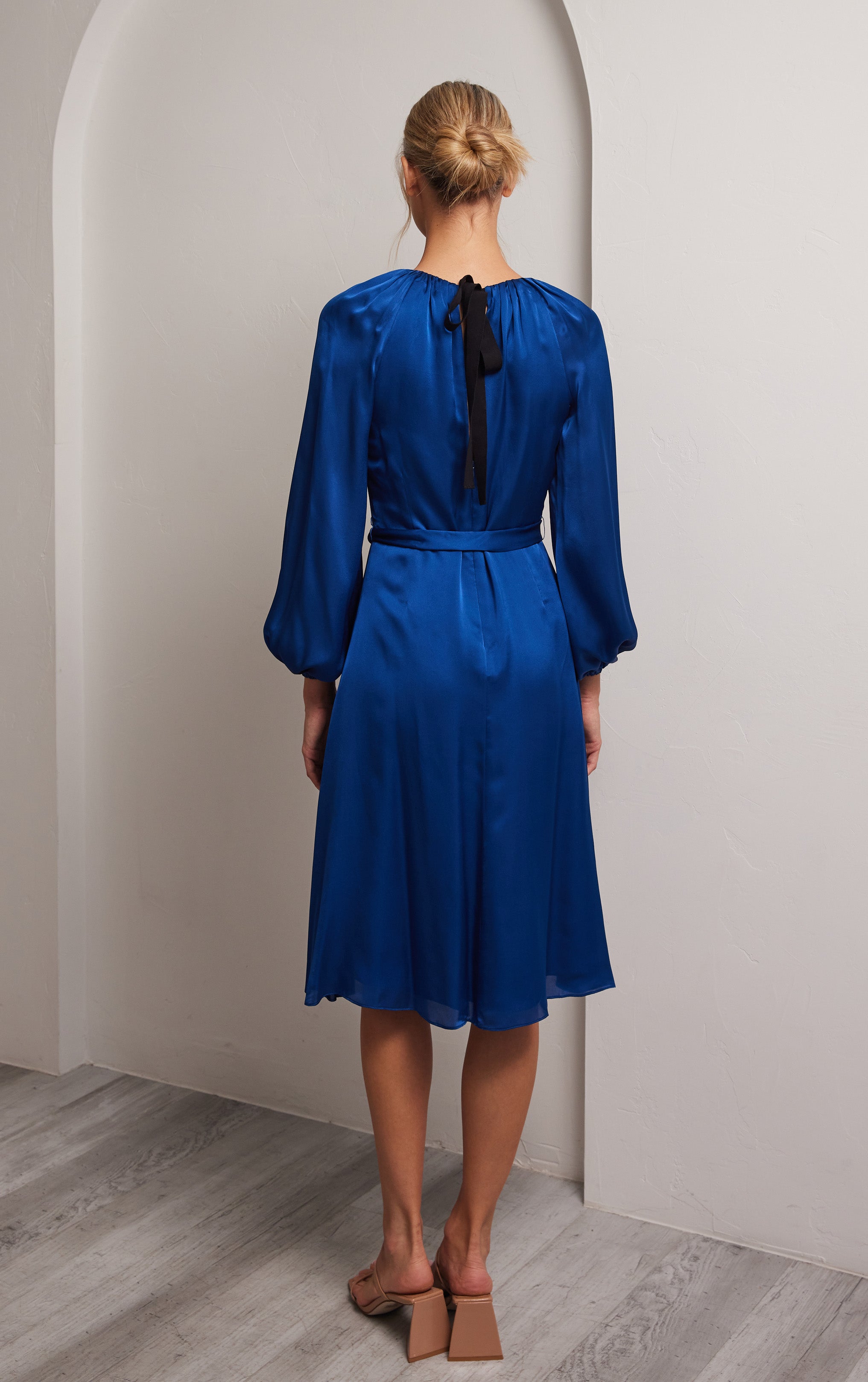 woman standing profile back view blue puff sleeve silk dress with rusched neck