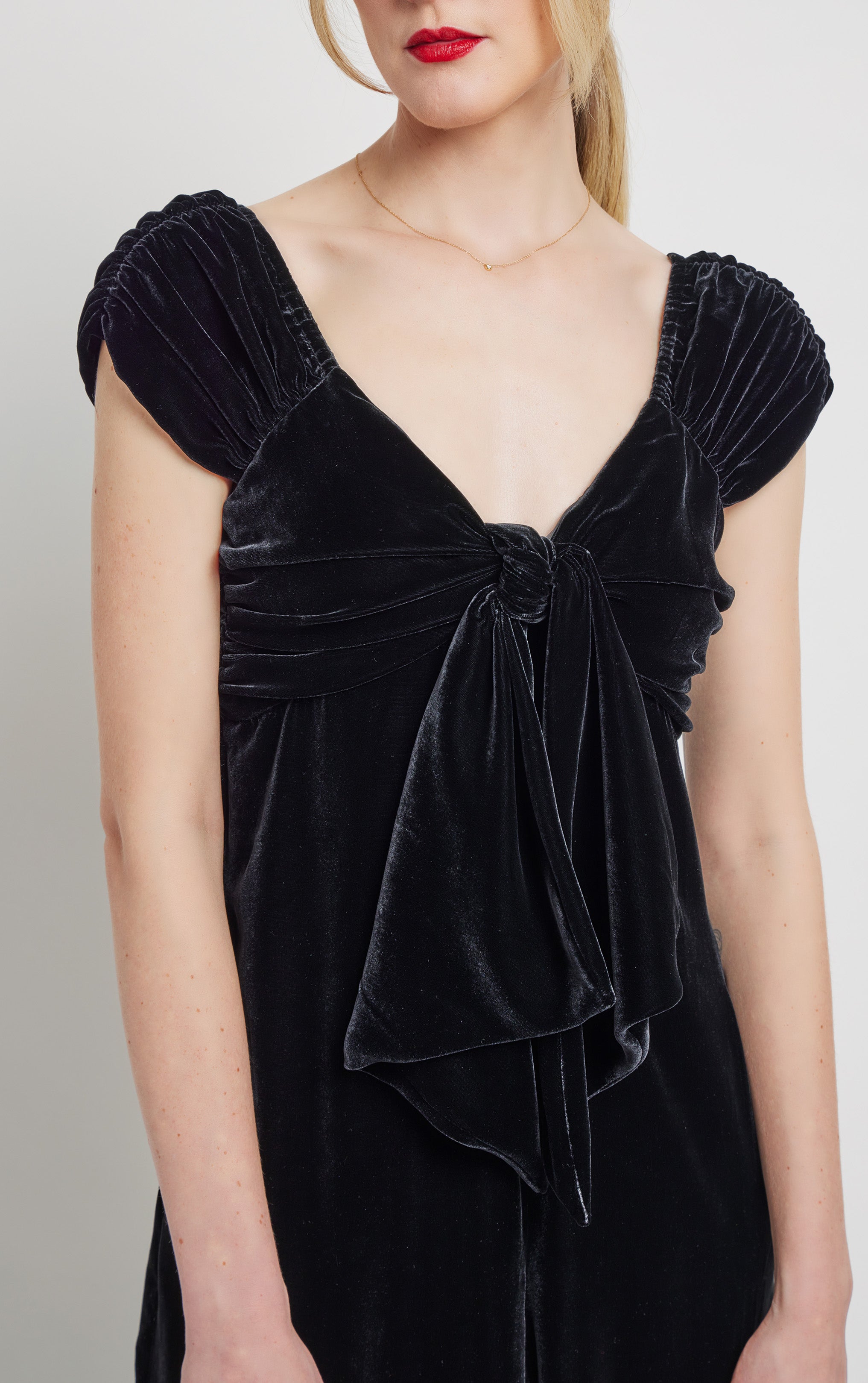 close up front profile of woman wearing silk velvet black jumpsuit with front bow