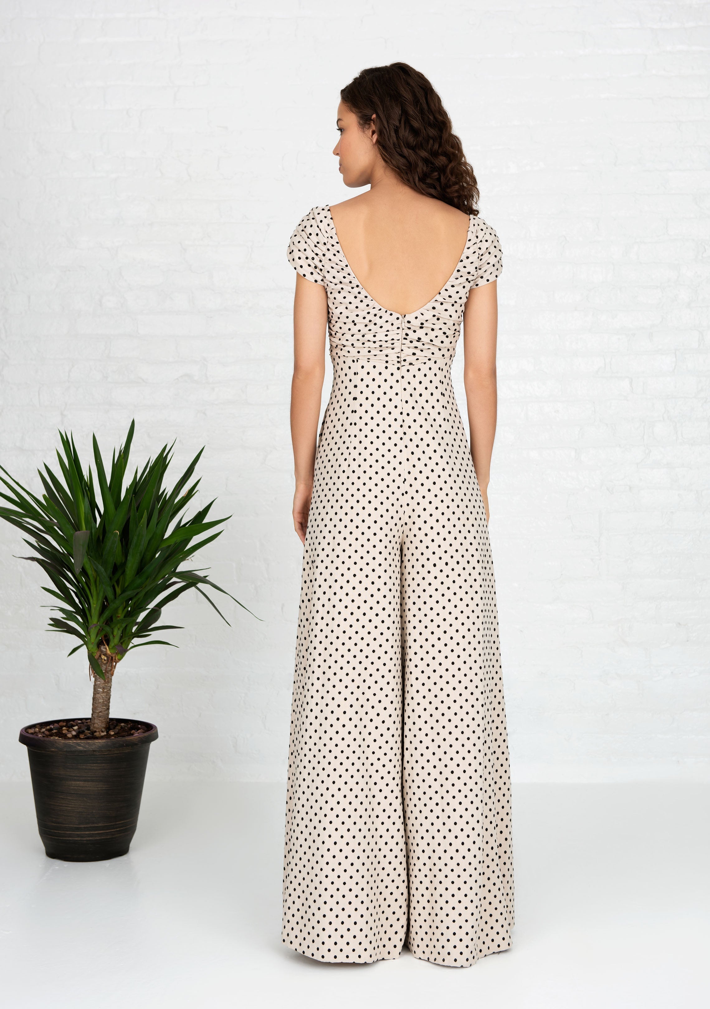 back view of woman wearing beige and black polka dot jumpsuit with tie up front