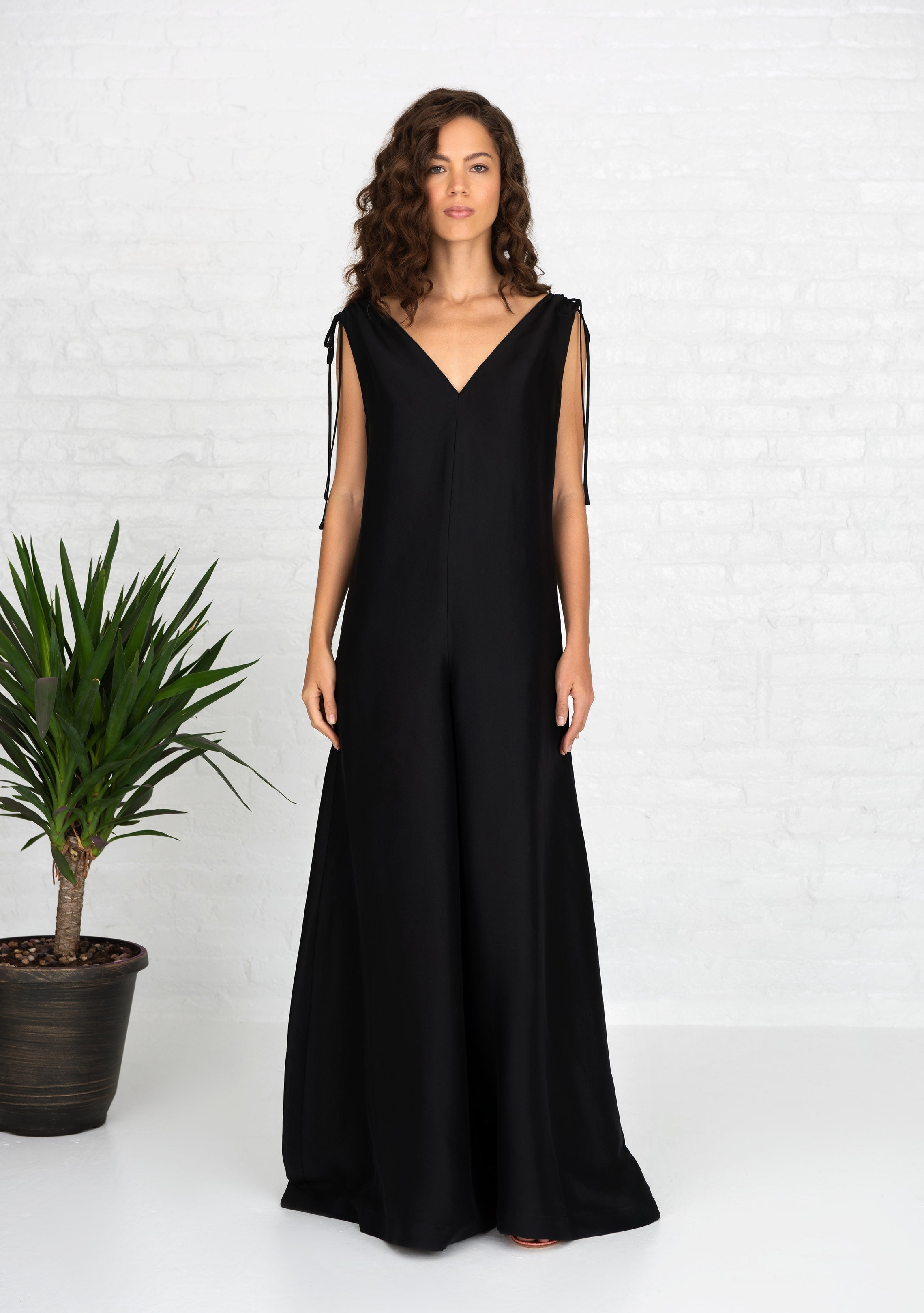woman wearing black sleeveless silk jumpsuit with side hand pockets