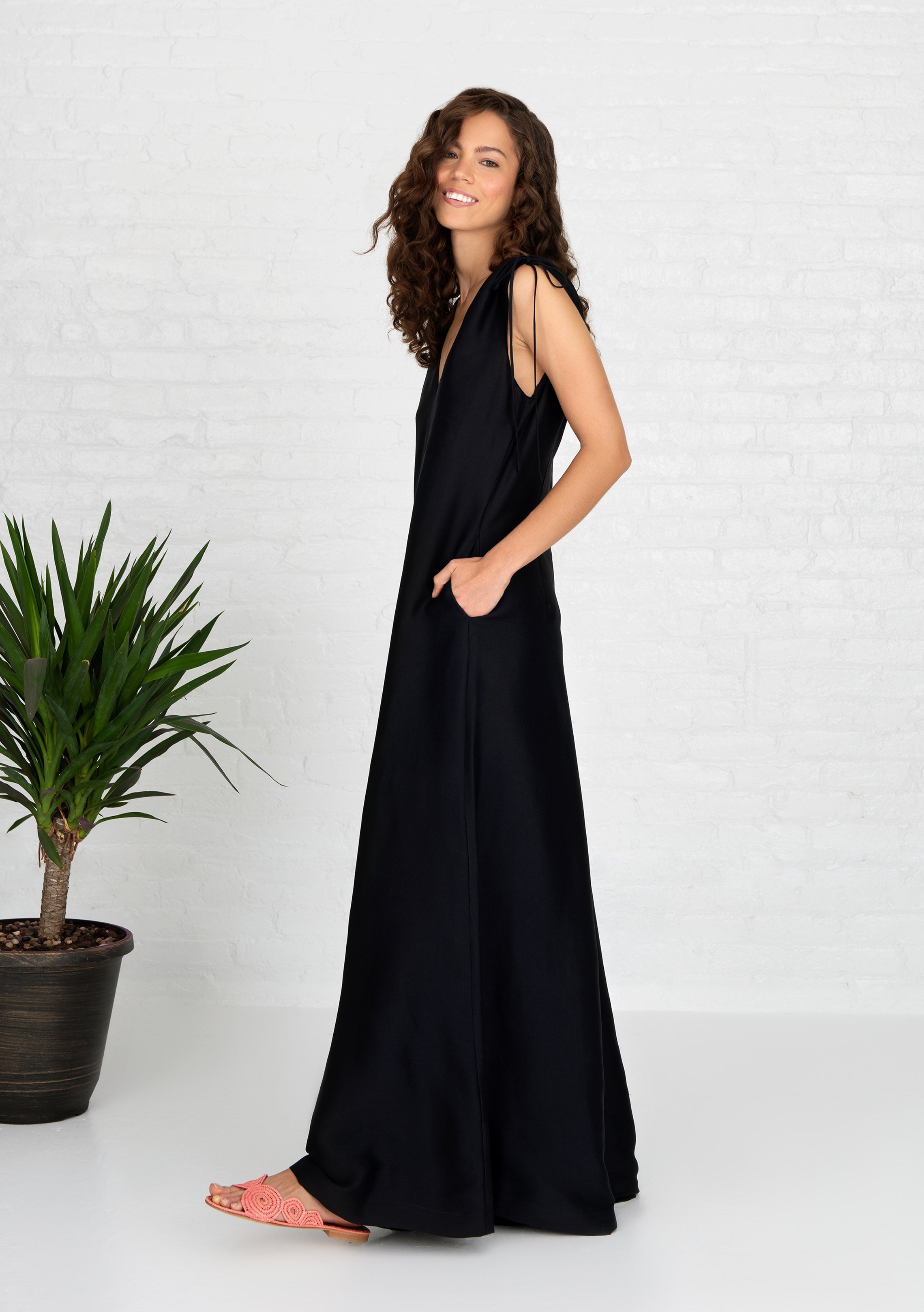 side profile of woman wearing black sleeveless relaxed fit silk jumpsuit with side hand pockets