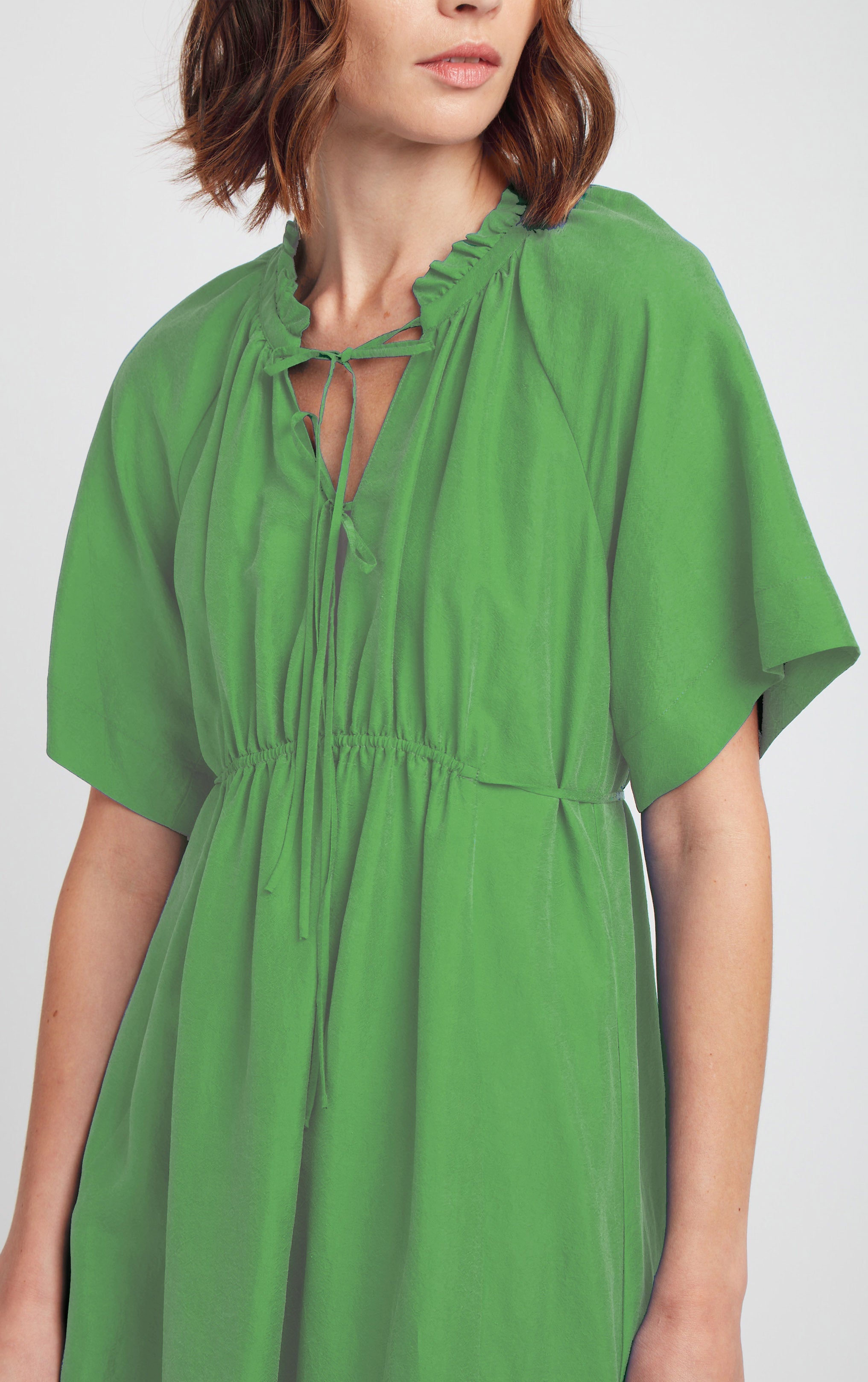 front view of woman wearing green short sleeved silk dress with ruffled neck trim and rusched neck