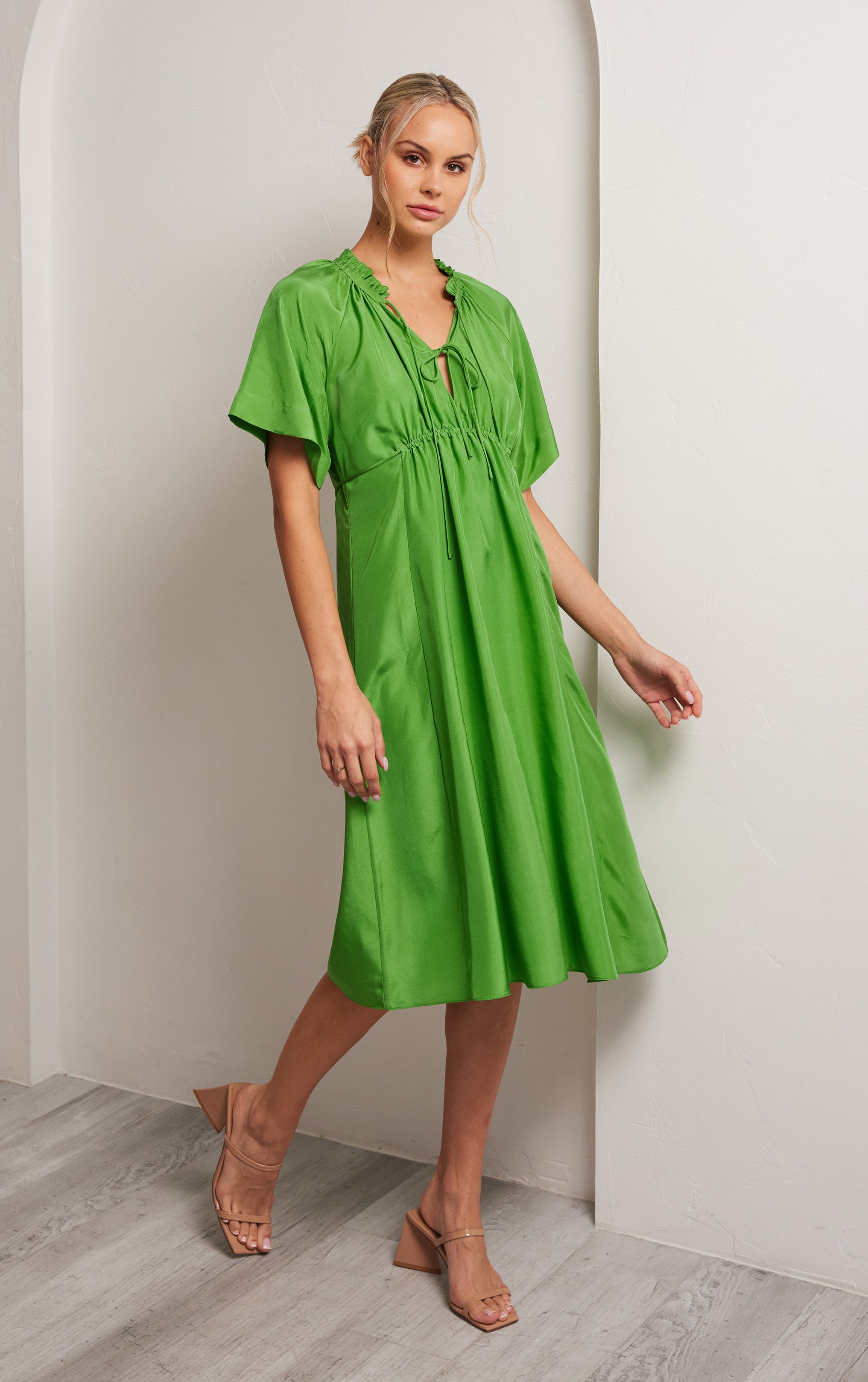 woman wearing green short sleeved silk dress with ruffled neck trim and rusched neck
