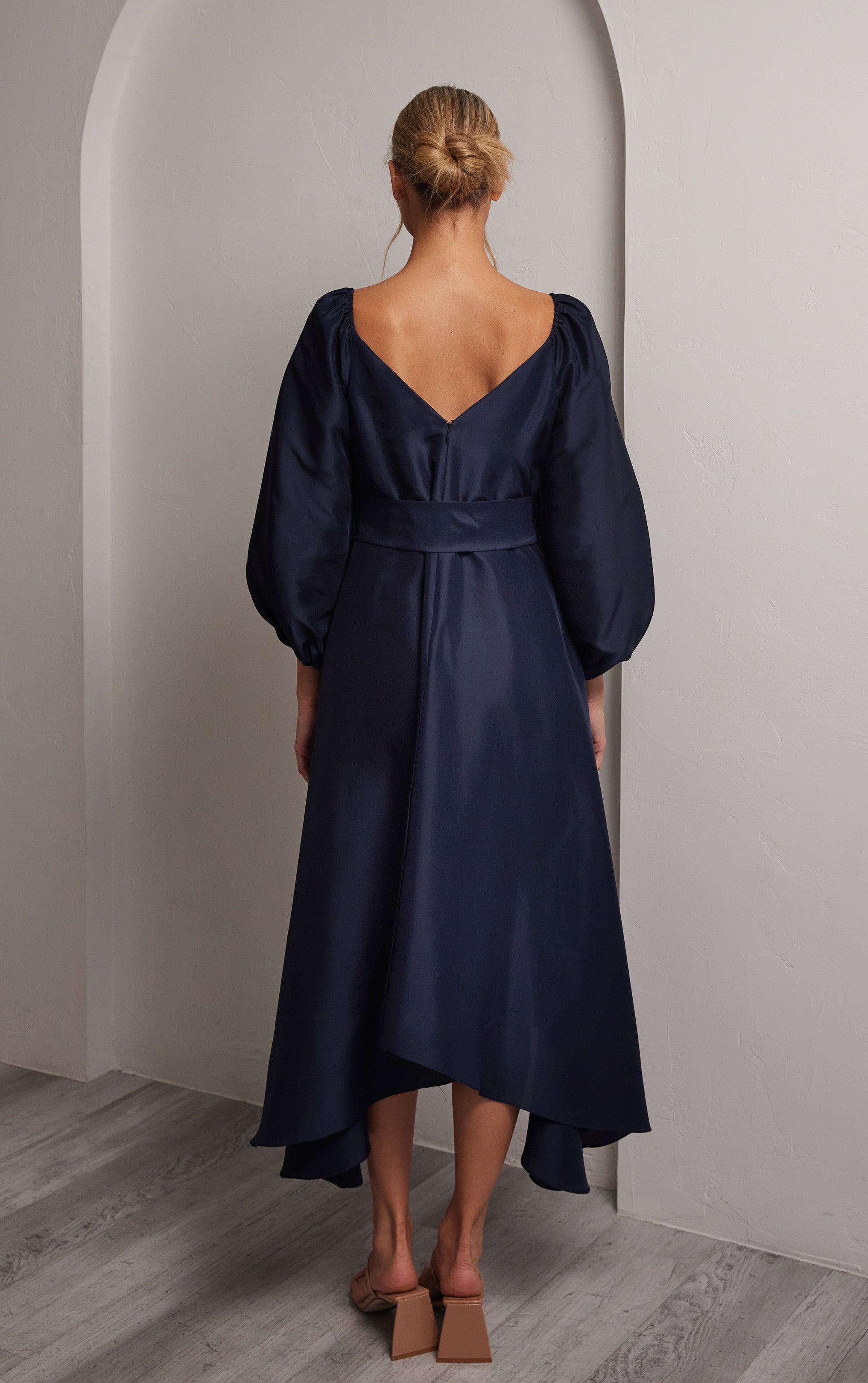 back view of woman wearing silk navy dress with puffed sleeves and tie at front