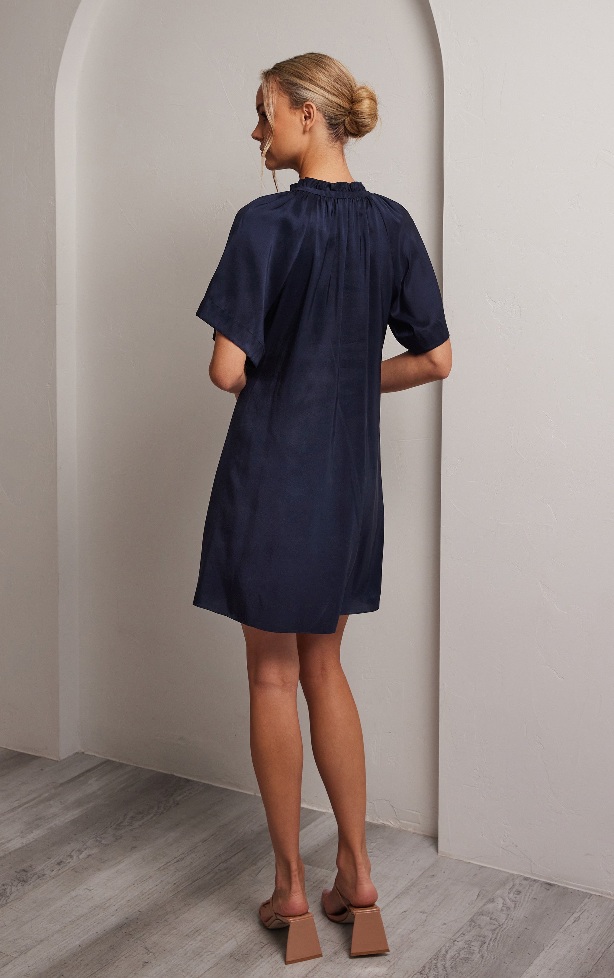 woman standing back view of navy short sleeved silk dress with ruffled neck and silhouette cut