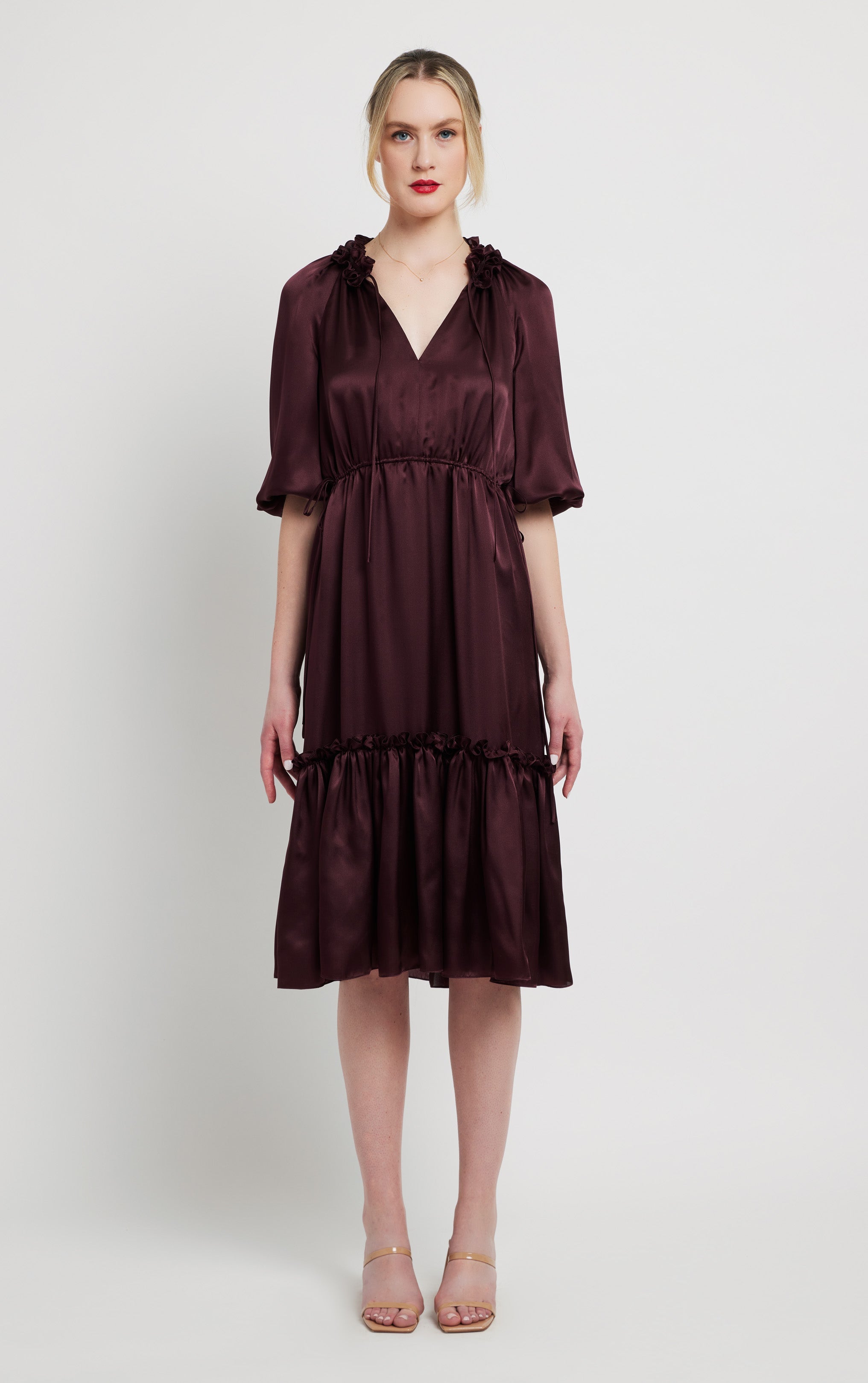 woman standing wearing burgundy silk dress with invisible zipper ruffled neck and puffed sleeves