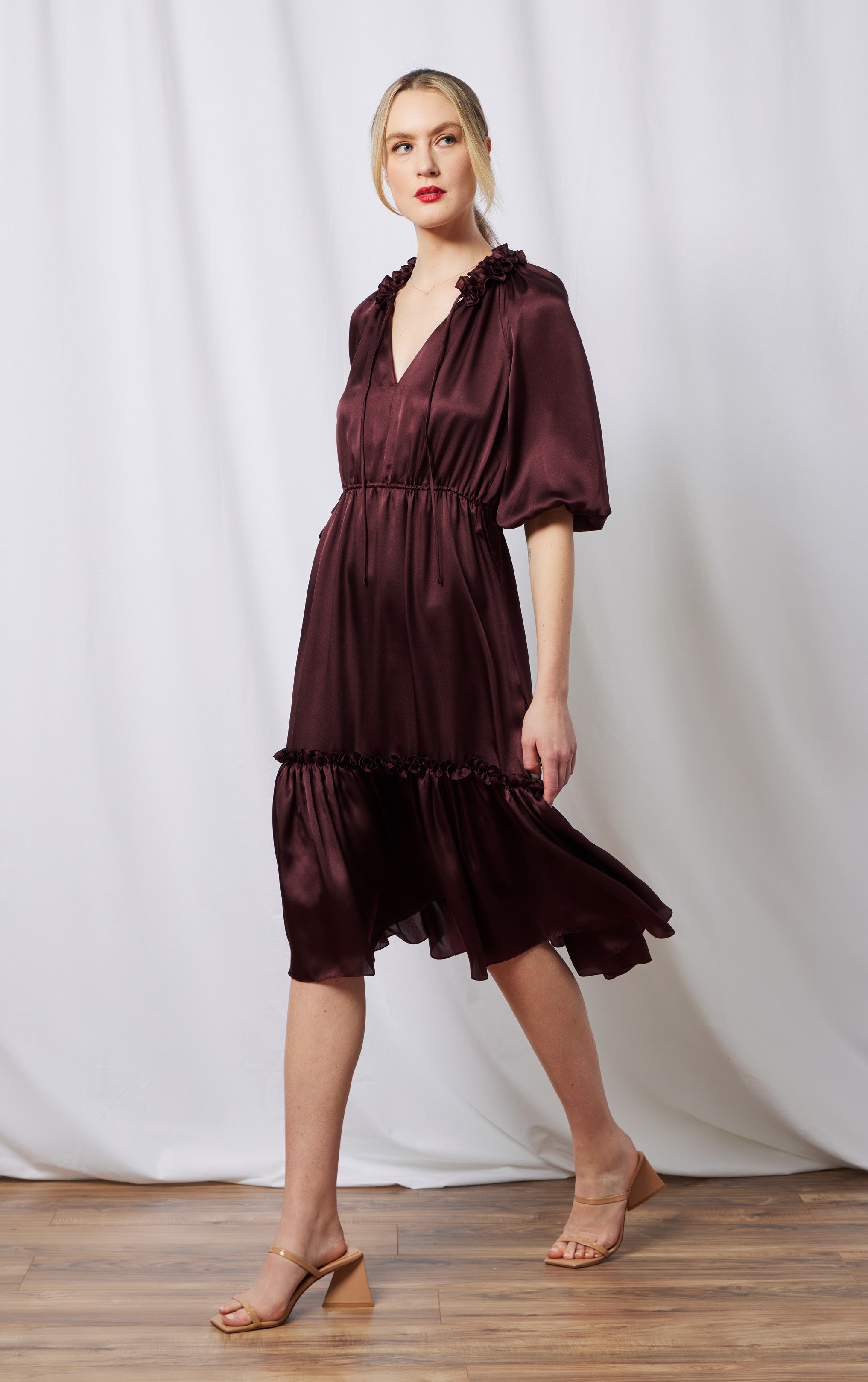 front view of woman wearing burgundy silk dress with invisible zipper ruffled neck and puffed sleeves